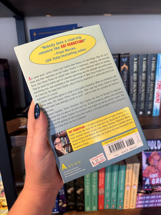 A hand holds the back cover for the novel 'Star Shipped' by Cat Sebastian, black text overlays a blue background for the blurb. 