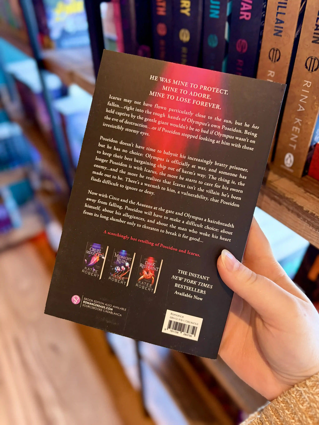 A hand holding the back of a paperback copy of the book 'Sweet Obsession' by Katee Robert. It is featuring a glowing pink and red spiral shell on a dark background with white and green title text.