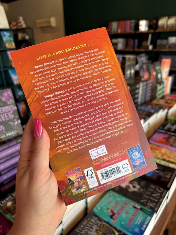 A hand with pink nail polish holding the back of a copy of 'Take a Chance, Sasha Sinclair' featuring an autumnal forest and white text.