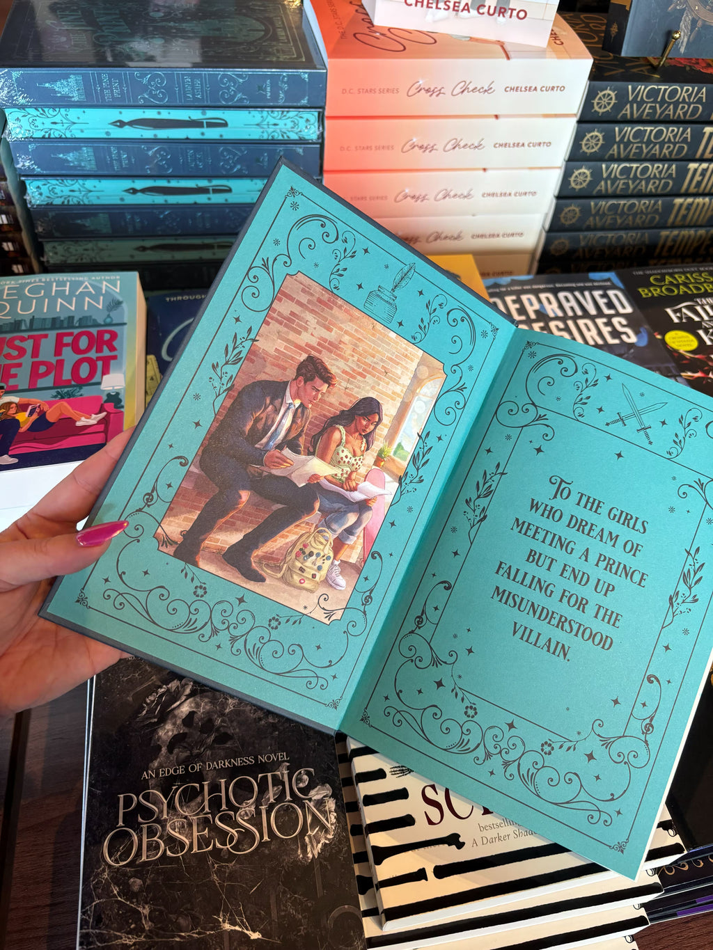 A hand with pink nail polish holds a copy of the special edition version of 'The Fine Print' by Lauren Asher in a bookstore with other books blurry in the background. The front end pages feature an illustration of the main characters sitting on a bench reading over pieces of paper on one side, and the book dedication in decorative text on the other side.