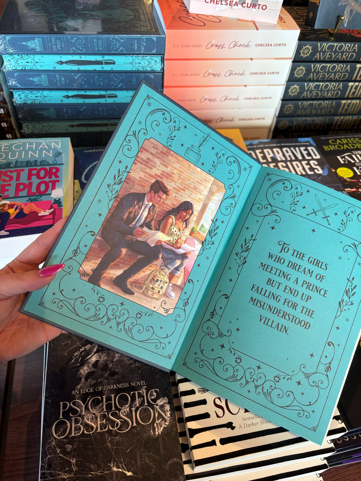 A hand with pink nail polish holds a copy of the special edition version of 'The Fine Print' by Lauren Asher in a bookstore with other books blurry in the background. The front end pages feature an illustration of the main characters sitting on a bench reading over pieces of paper on one side, and the book dedication in decorative text on the other side.