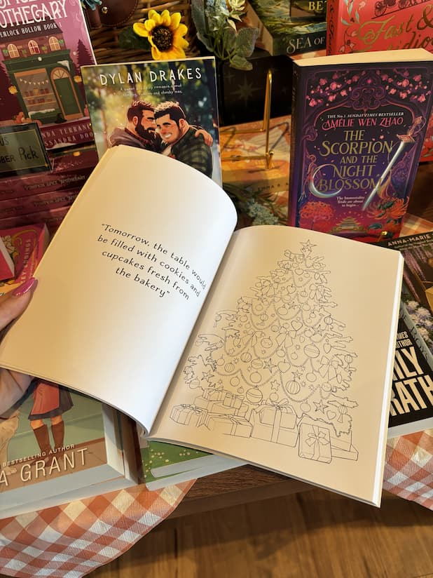 A hand with pink nail polish holding open a copy of 'The Gingerbread Bakery Coloring & Sticker Book' showing a quote on the left page and an illustration of a decorated Christmas Tree.