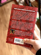A hand holds the back of the book 'The Kings of Kearny' by Navessa Allen in front of a blurred bookshelf background. The cover is red and black with white text.