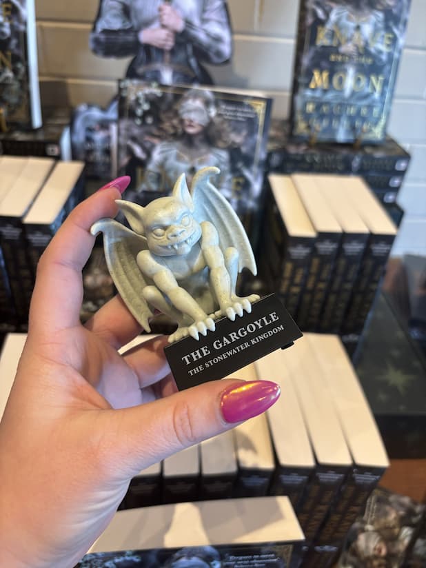 A hand with pink nail polish holding a gargoyle figurine. It sits upon a platform that reads 'The Gargoyle' in large text and 'The Stonewater Kingdom' in smaller text under that.