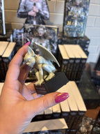 A hand with pink nail polish holding a gargoyle figurine to the side. It sits upon a platform that reads 'The Gargoyle' in large text and 'The Stonewater Kingdom' in smaller text under that.