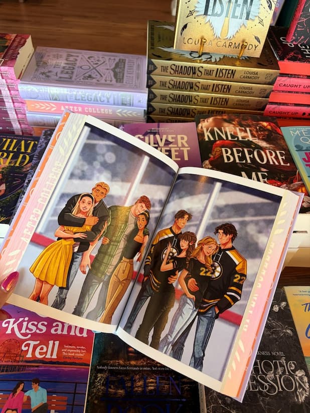 A hand with pink nail polish holds a hardcover special edition of 'The Legacy' by Elle Kennedy open, displaying a colorful illustration of five young adults standing at an ice rink.