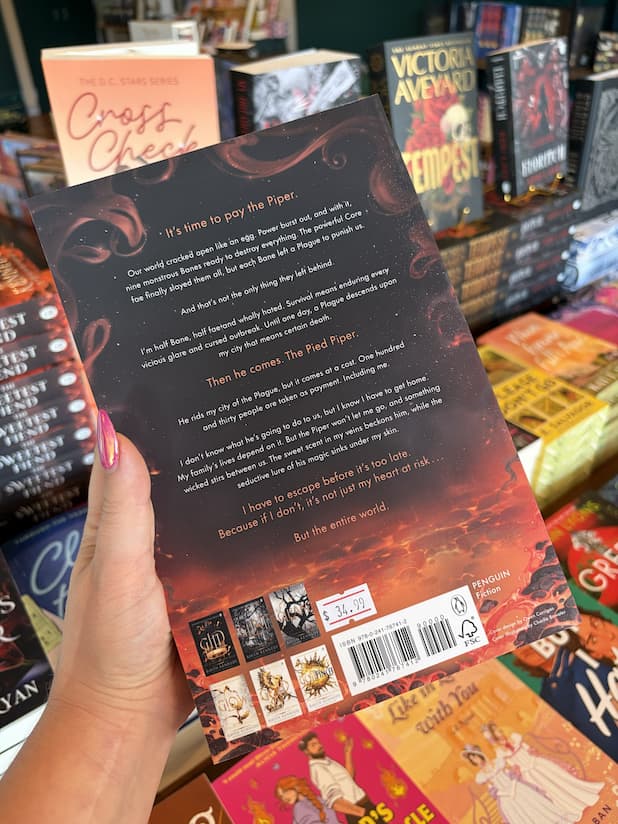 A hand with pink nail polish holds the back of a copy of 'The Sweetest Fiend' by Raven Kennedy, featuring a dark cover with smoke, lava, and white and orange text.