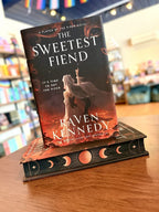 A small stack of the special edition of 'The Sweetest Fiend' by Raven Kennedy, showing a dark fantasy illustration of a hooded figure with a glowing staff against a fiery red and black background, with sprayed edges featuring moon phases.