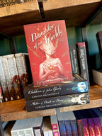 The book 'Daughter of No Worlds' by Carissa Broadbent is displayed upright on a wooden bookshelf, resting on top of two other books: 'Children of Fallen Gods' and 'Mother of Death and Dust'.