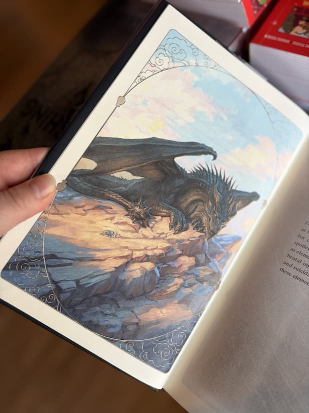 An open hardcover copy of 'Threshing Day' by Rebecca Yarros, showing a large, black dragon sitting atop a stony mountain.