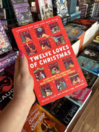 A hand with pink nail polish holding a copy of 'The Twelve Loves of Christmas' featuring a bright red background with illustrated holiday scenes in window frames and large white title text.