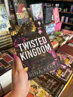 A hand with pink nail polish holds a copy of the book 'Twisted Kingdom' by Rina Kent in a bookshop, with other book displays visible in the background. Metallic font overlaps a maroon, pink, black and mustard coloured floral pattern with a king and queen chess piece in opposite corners.