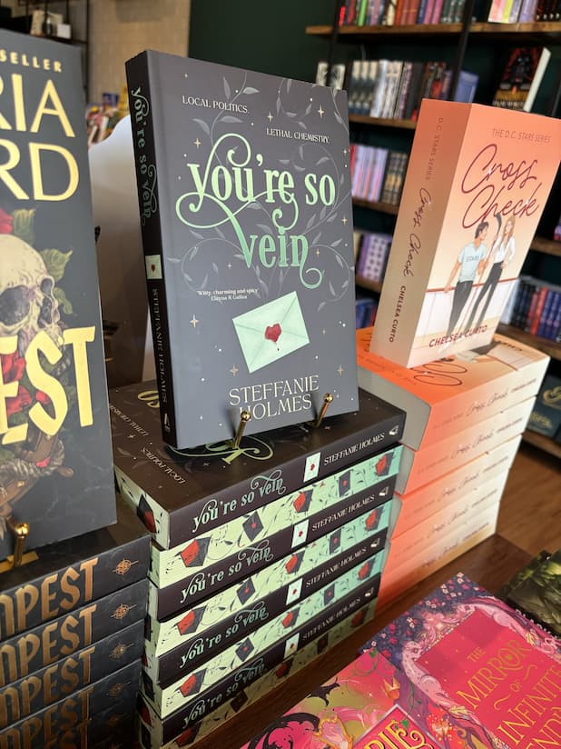 A stack of 'You're So Vein' by Steffanie Holmes, featuring a black cover with green vines and a letter with a heart-shaped wax seal, with matching sprayed edges.